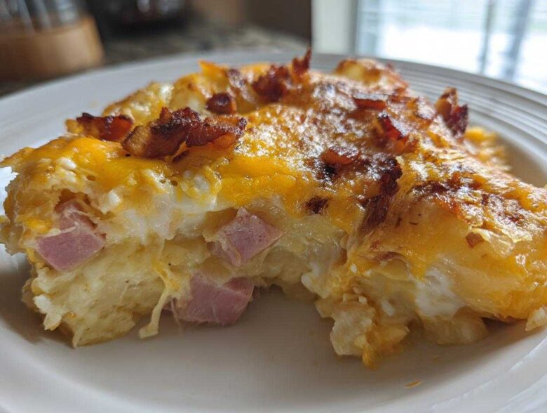 Close-up of a serving of scalloped potatoes and ham, topped with melted cheddar cheese and crispy bacon pieces.