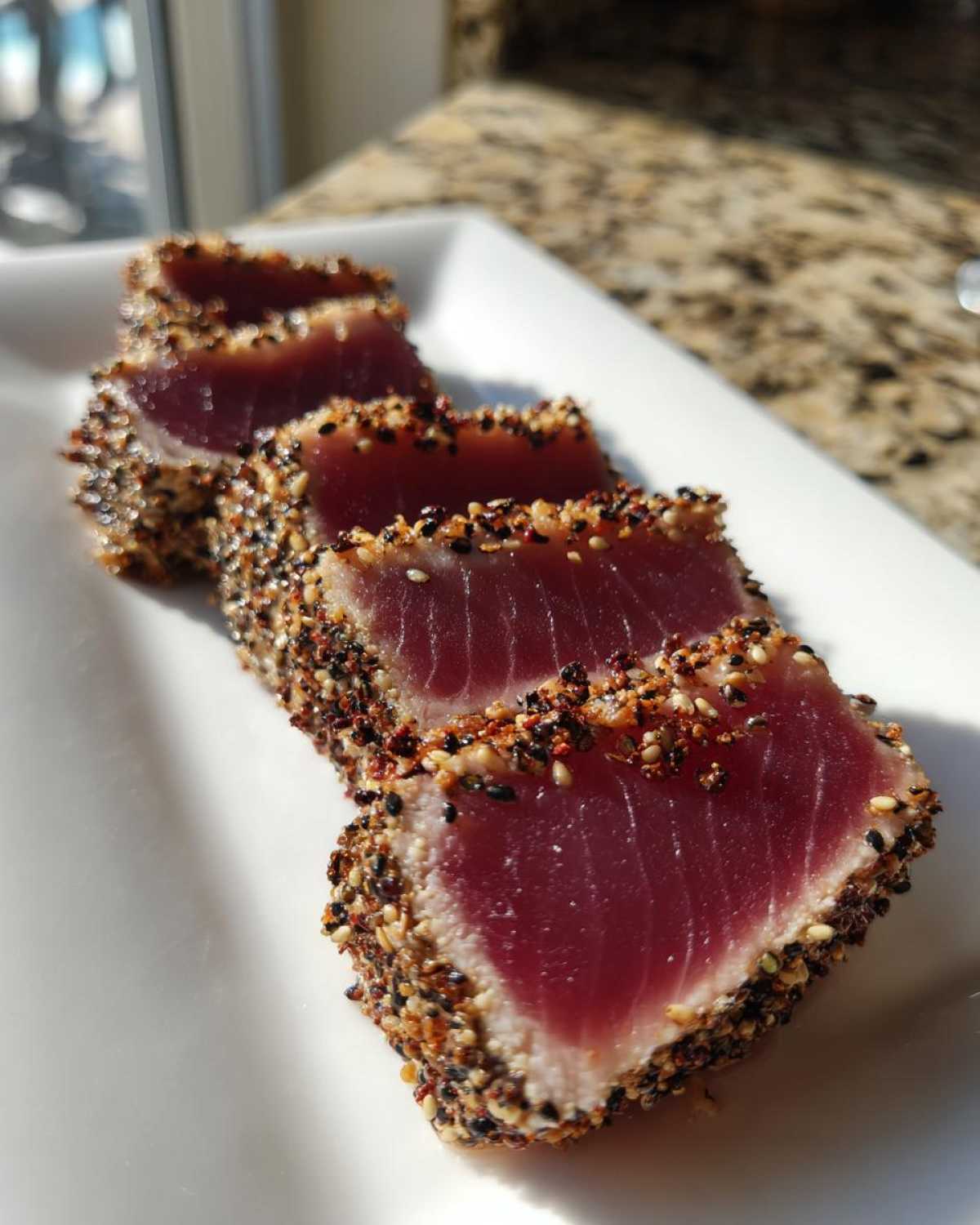 Four slices of perfectly seared ahi tuna, crusted with black and white sesame seeds, resting on a white plate.