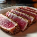Slices of perfectly seared tuna steak, showing a rare, bright pink center and a cracked pepper crust, ready to serve.