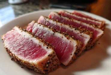 Slices of perfectly seared tuna steak, showing a rare, bright pink center and a cracked pepper crust, ready to serve.