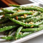 A close-up of bright green beans seasoned with garlic and salt, ready to eat.