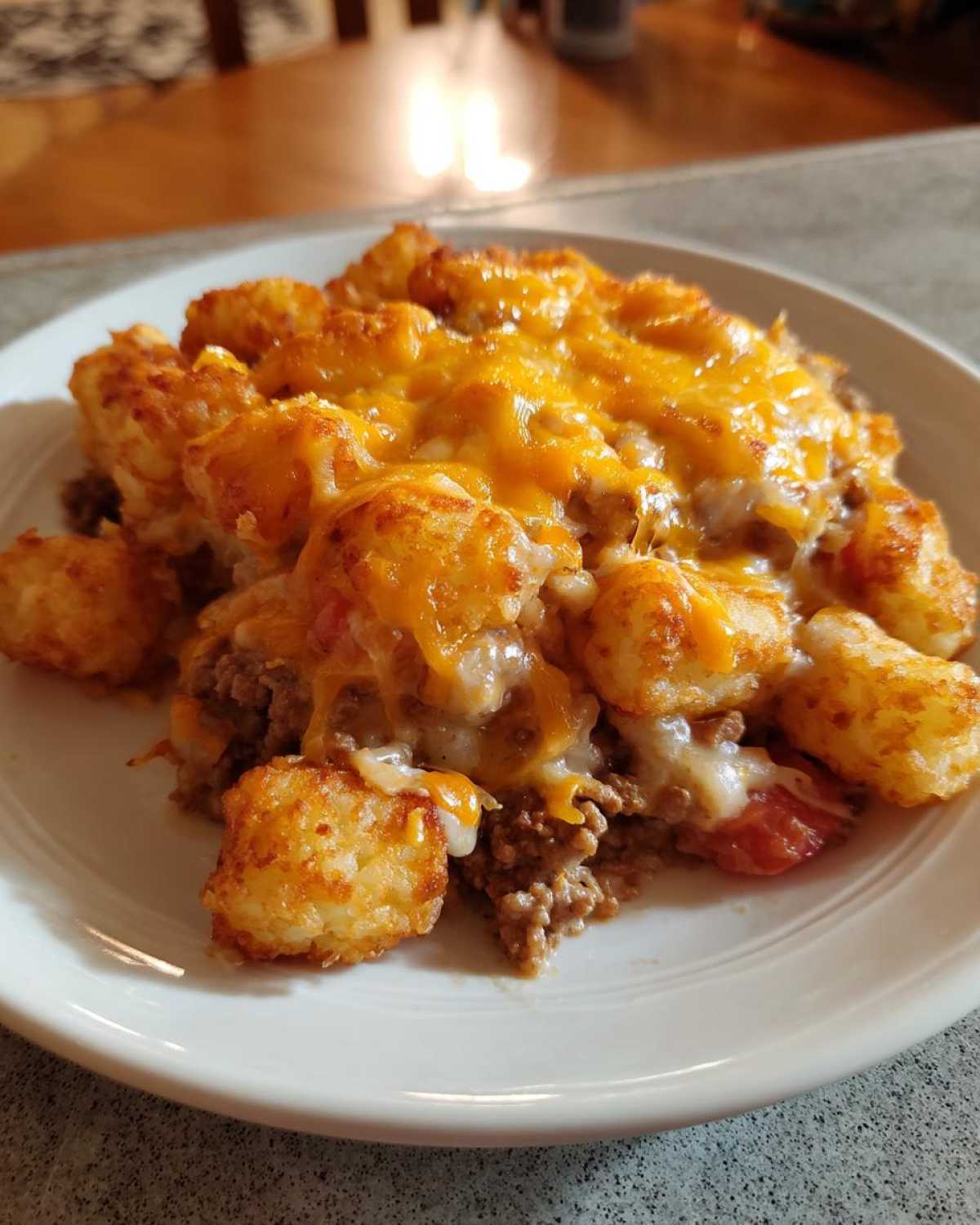 A close-up serving of tater tot casserole featuring crispy tots, ground beef, and melted cheddar cheese on a white plate.
