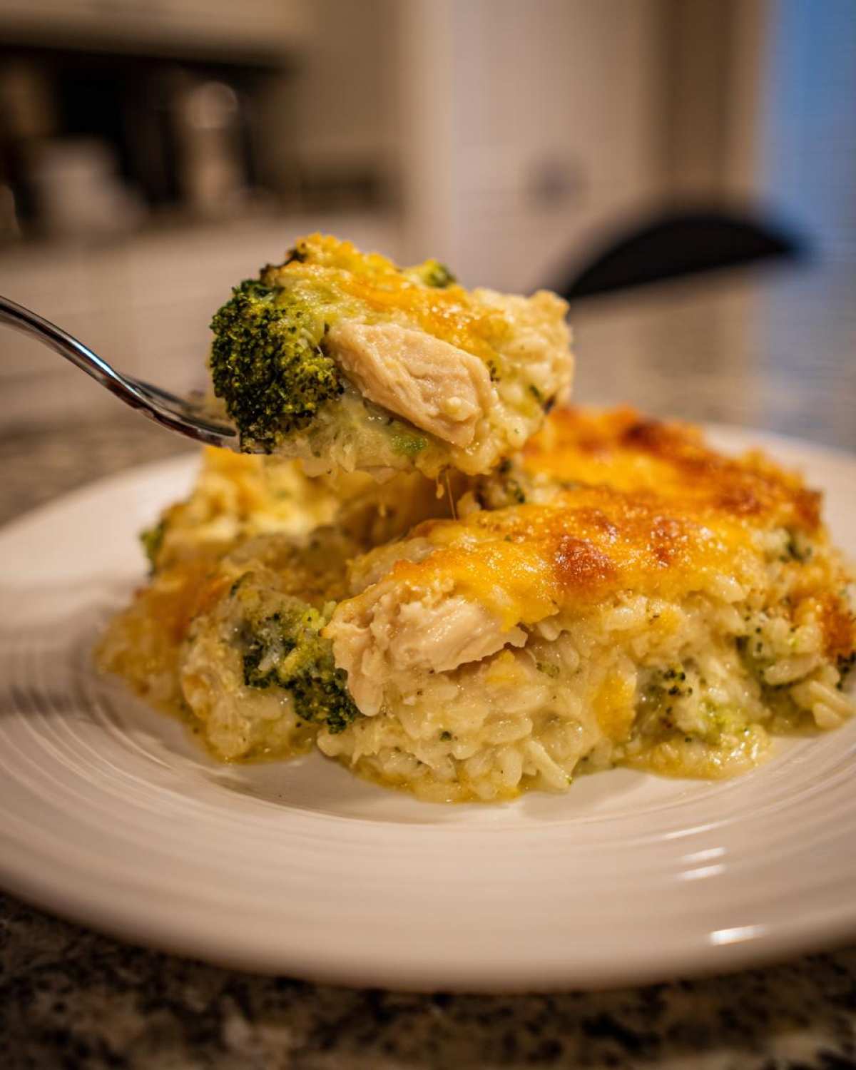 A fork lifts a bite of creamy chicken broccoli rice casserole topped with melted cheddar cheese.