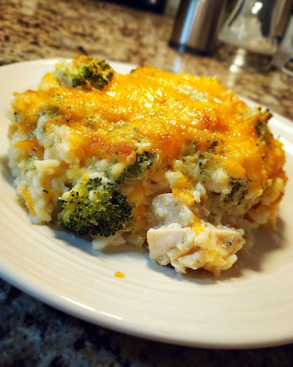 A close-up serving of creamy chicken broccoli rice casserole topped with melted cheddar cheese.
