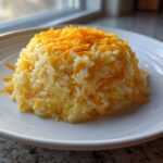 A mound of fluffy white rice mixed with melted and shredded cheddar cheese, served on a white plate, showcasing easy cheesy rice.