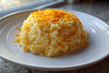 A mound of fluffy white rice mixed with melted and shredded cheddar cheese, served on a white plate, showcasing easy cheesy rice.