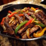 Close-up of sizzling steak fajitas with sliced peppers and onions served hot in a cast iron skillet.