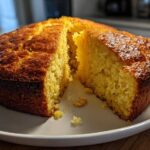 A freshly baked, golden-brown skillet cornbread with a wedge cut out, showing its moist interior texture.