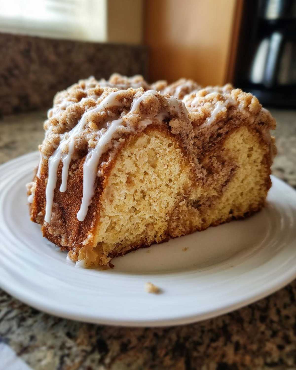 A thick slice of moist coffee cake with a cinnamon streusel topping and white glaze drizzle.