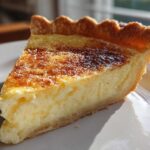 A close-up slice of golden-brown baked egg custard with a flaky crust on a white plate.