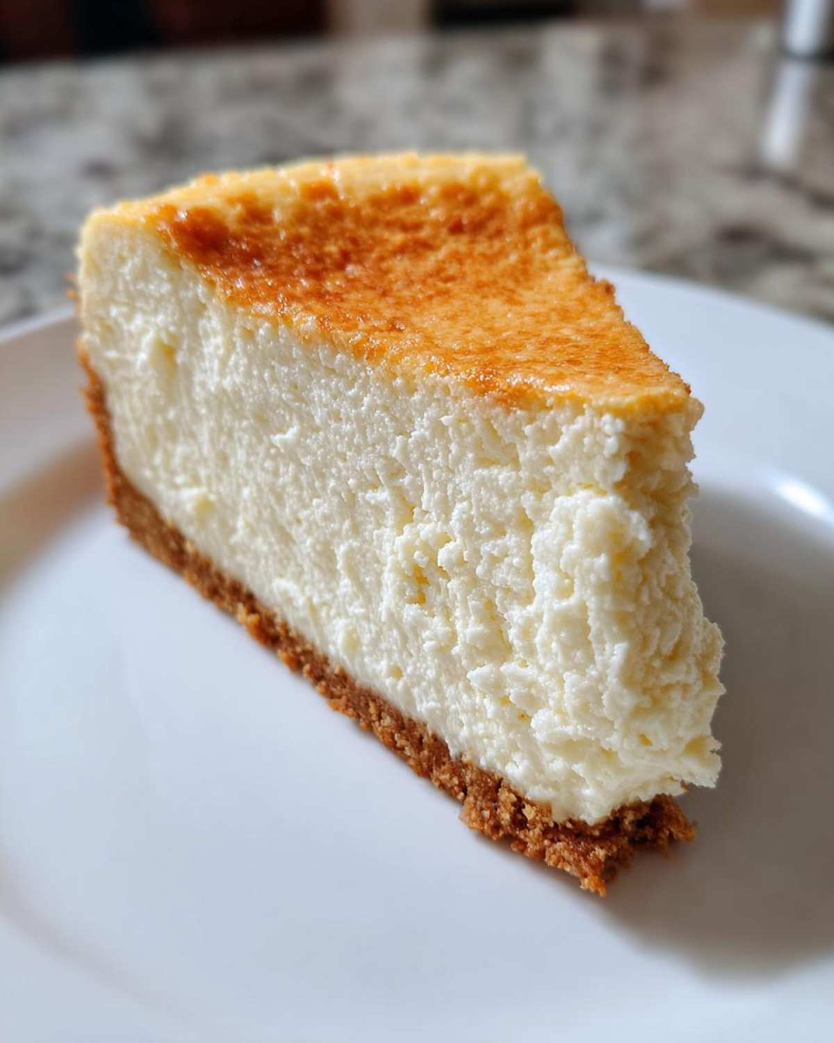A perfect slice of creamy Protein Cheesecake with a golden-brown top and graham cracker crust on a white plate.