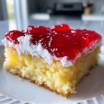 Close-up of a moist slice of jello poke cake topped with white whipped cream and bright red gelatin.