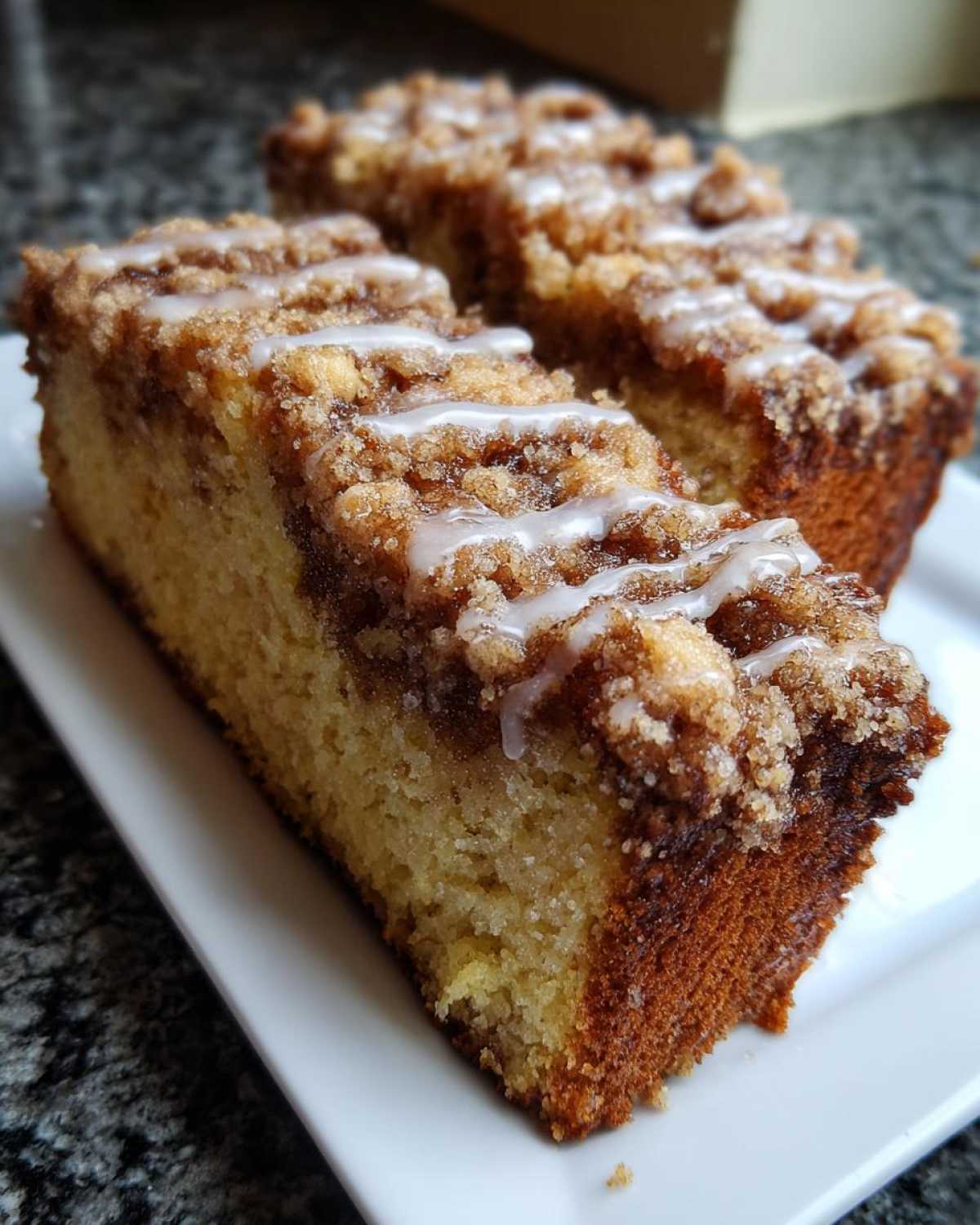 Two slices of moist coffee cake featuring a thick cinnamon streusel topping and a light vanilla glaze drizzle.