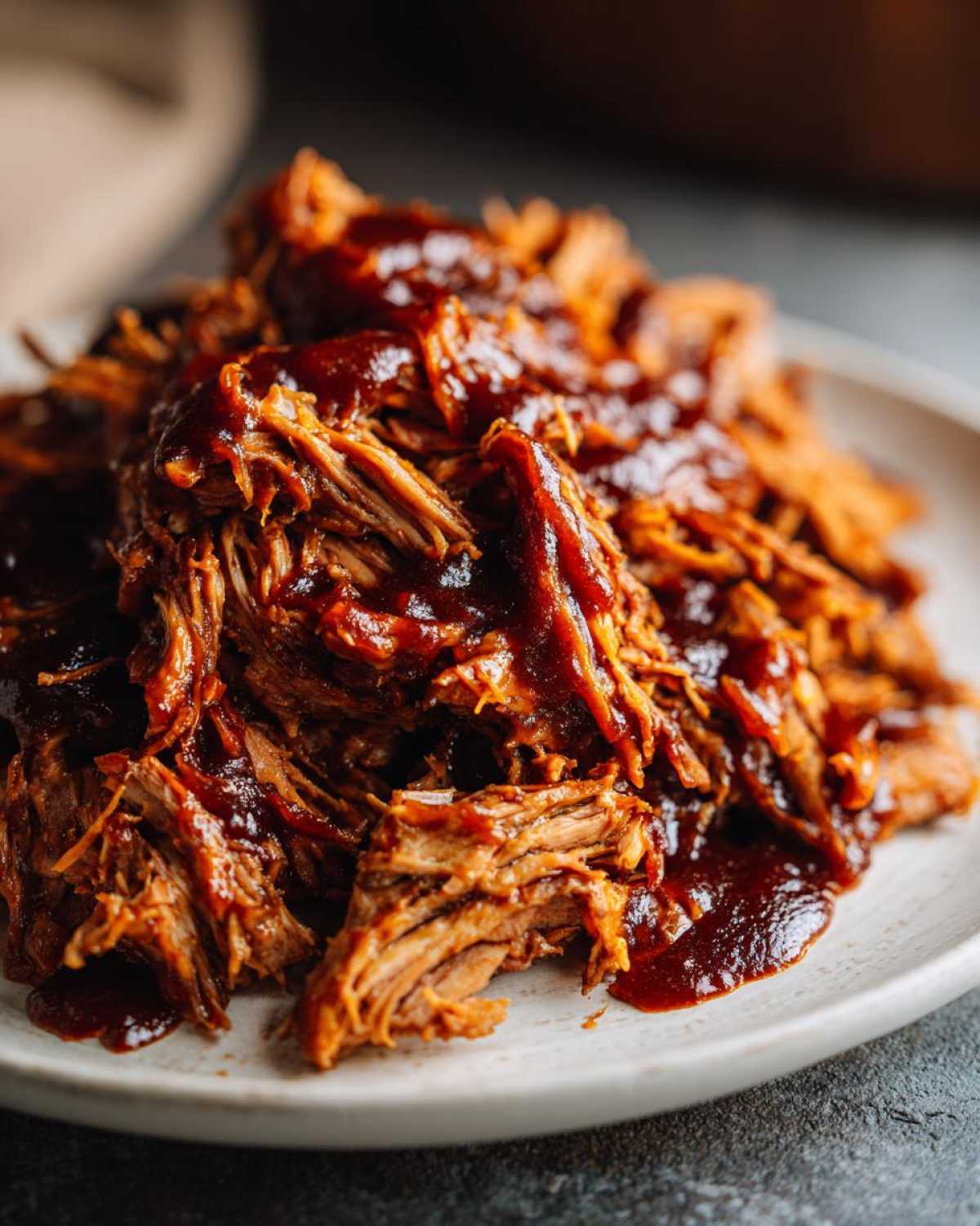 Close-up of tender, shredded Slow Cooker Pulled Pork generously coated in rich barbecue sauce on a white plate.