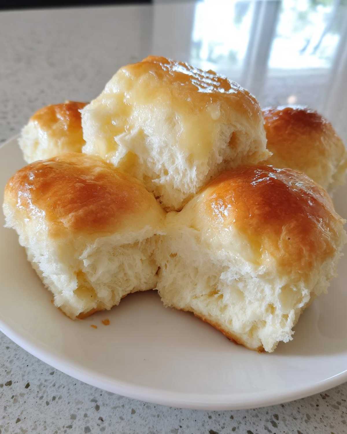 Close-up of four fluffy dinner rolls brushed with melted butter, one roll pulled apart.