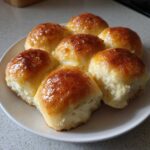 Close-up of six golden brown and glossy dinner rolls baked together on a white plate.