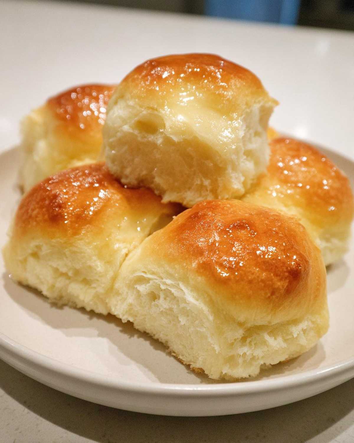 A stack of four golden-brown, soft dinner rolls glistening with melted butter or glaze.