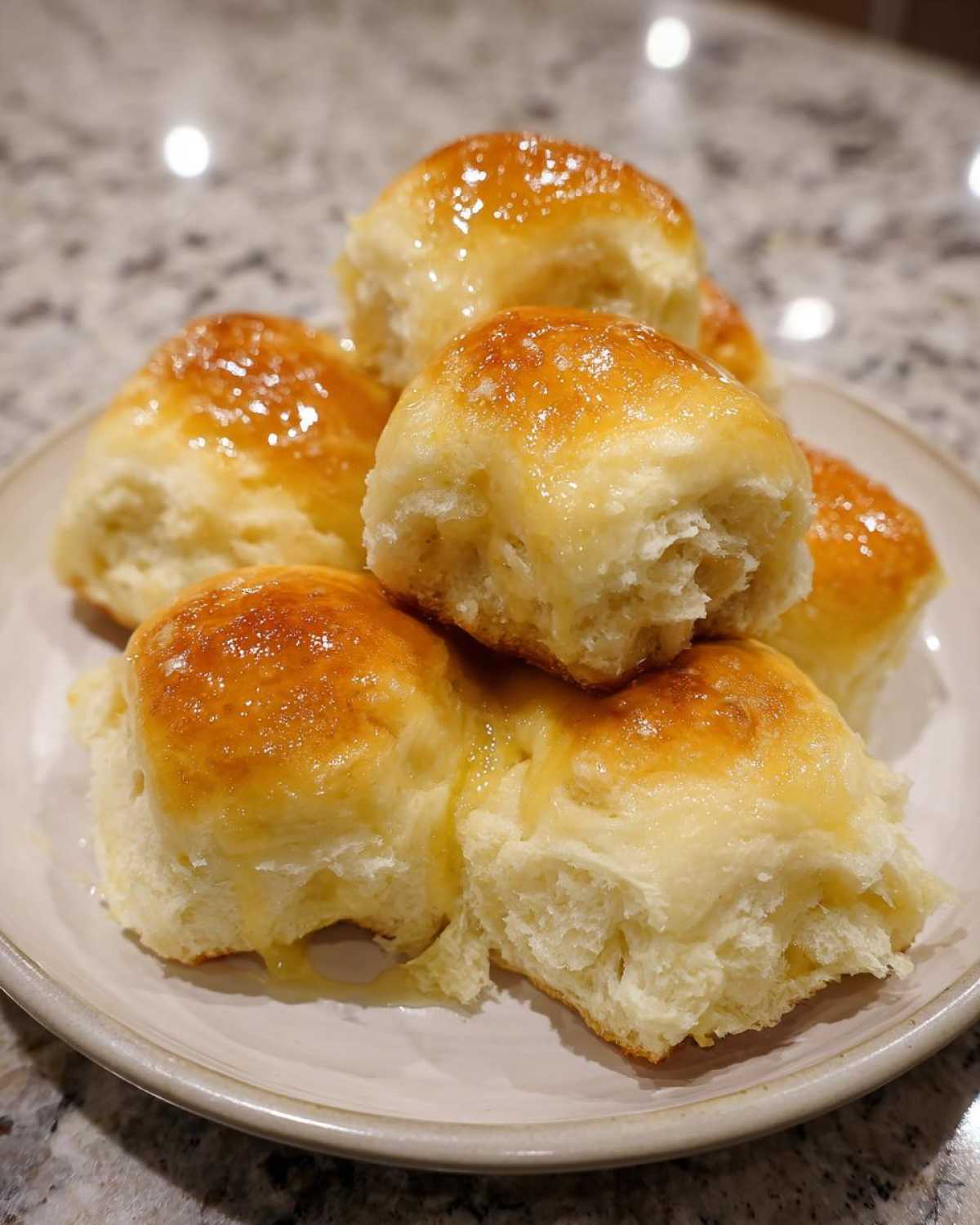 A stack of fluffy, golden-brown dinner rolls generously brushed with melted butter or glaze.