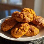 A stack of soft, orange-colored persimmon cookies sprinkled with sugar on a white plate.