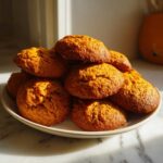 A warm stack of freshly baked, soft persimmon cookies piled high on a light-colored plate.