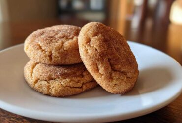 A stack of three soft, cinnamon-sugar coated pumpkin snickerdoodle cookies resting on a white plate.