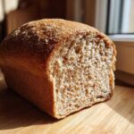 A freshly baked loaf of whole wheat bread, cut to show its soft, airy crumb texture.