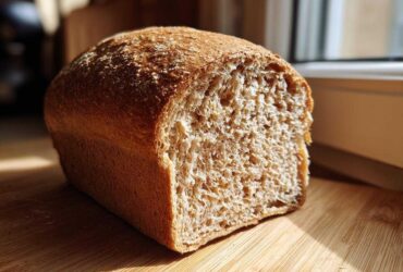 A freshly baked loaf of whole wheat bread, cut to show its soft, airy crumb texture.