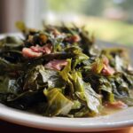 A close-up of tender, slow-cooked collard greens mixed with pieces of smoked ham on a white plate.