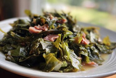 A close-up of tender, slow-cooked collard greens mixed with pieces of smoked ham on a white plate.