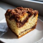 Close-up of a moist slice of sour cream coffee cake featuring a rich cinnamon swirl and crumbly streusel topping.