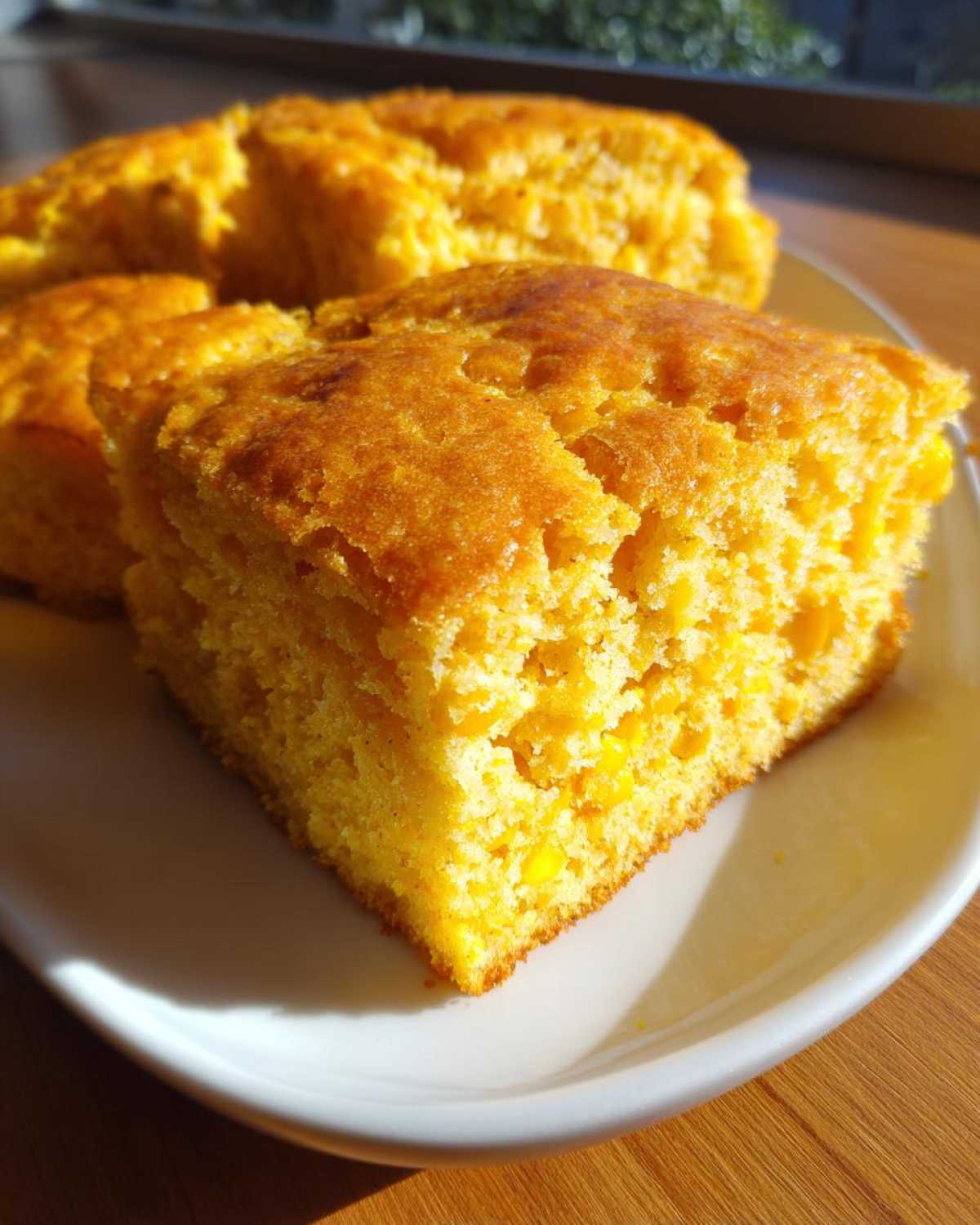 A close-up, golden-brown slice of moist sourdough cornbread served on a white plate.