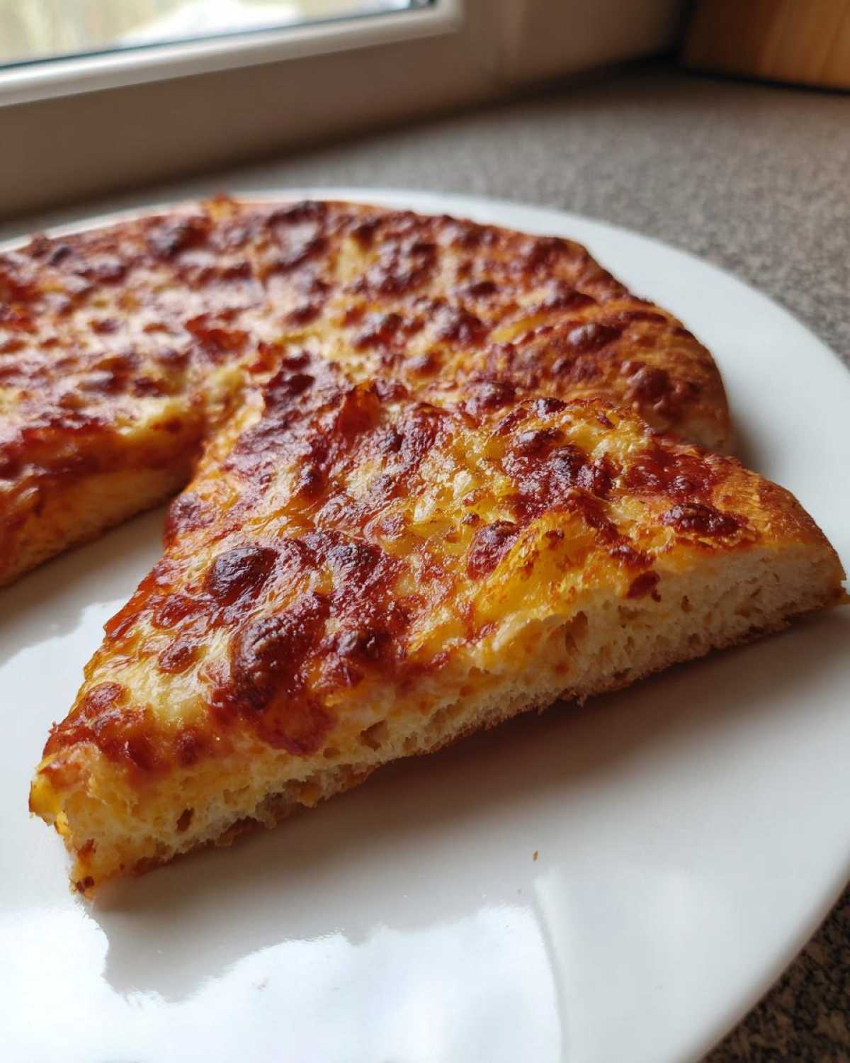 A slice of cheesy pizza made with sourdough discard pizza dough, showing a thick, airy crust.