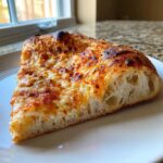 Close-up of a slice of cheesy pizza showing the airy, bubbly crust made from sourdough discard pizza dough.
