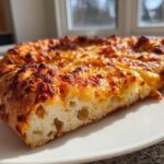Close-up of a slice of pizza made with sourdough discard pizza dough, showing airy crumb and bubbly, browned cheese.