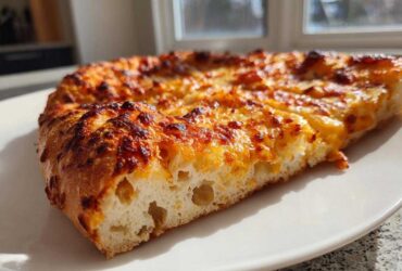 Close-up of a slice of pizza made with sourdough discard pizza dough, showing airy crumb and bubbly, browned cheese.