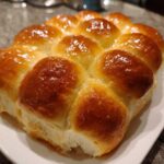 A cluster of soft, golden brown sourdough discard rolls with a shiny, buttery glaze served on a white plate.