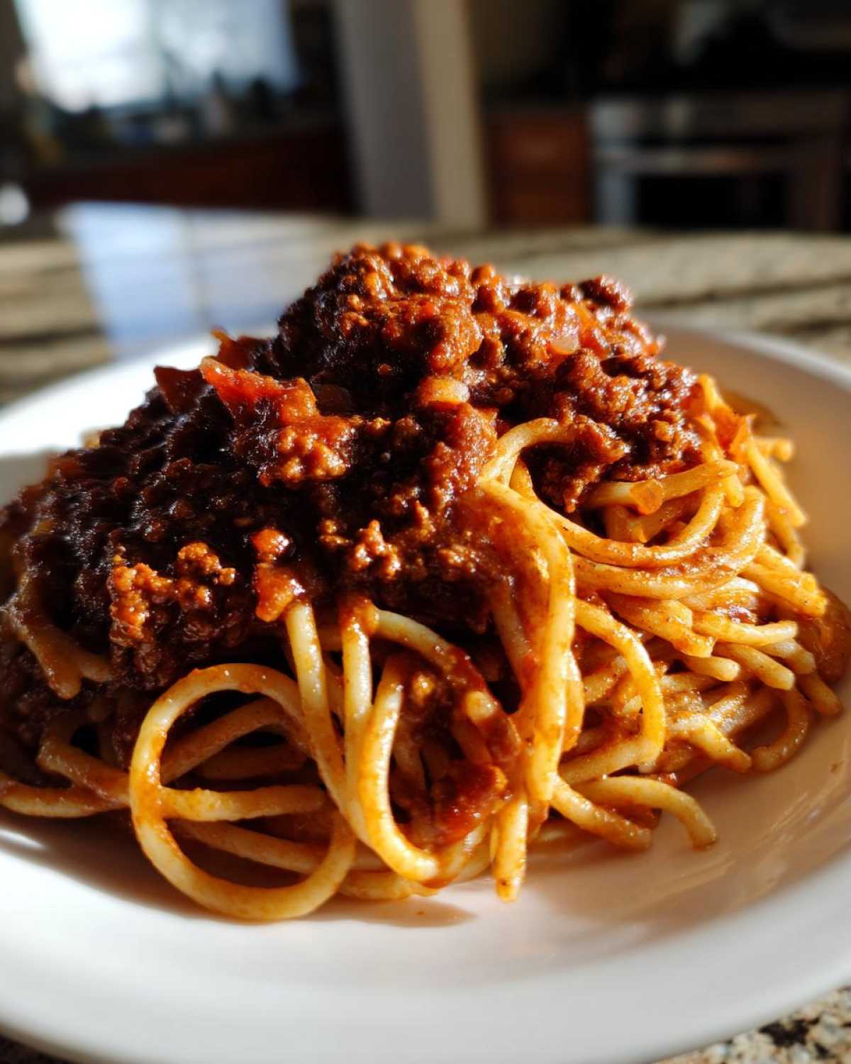 Close-up of spaghetti noodles generously topped with rich, thick bolognese sauce on a white plate.