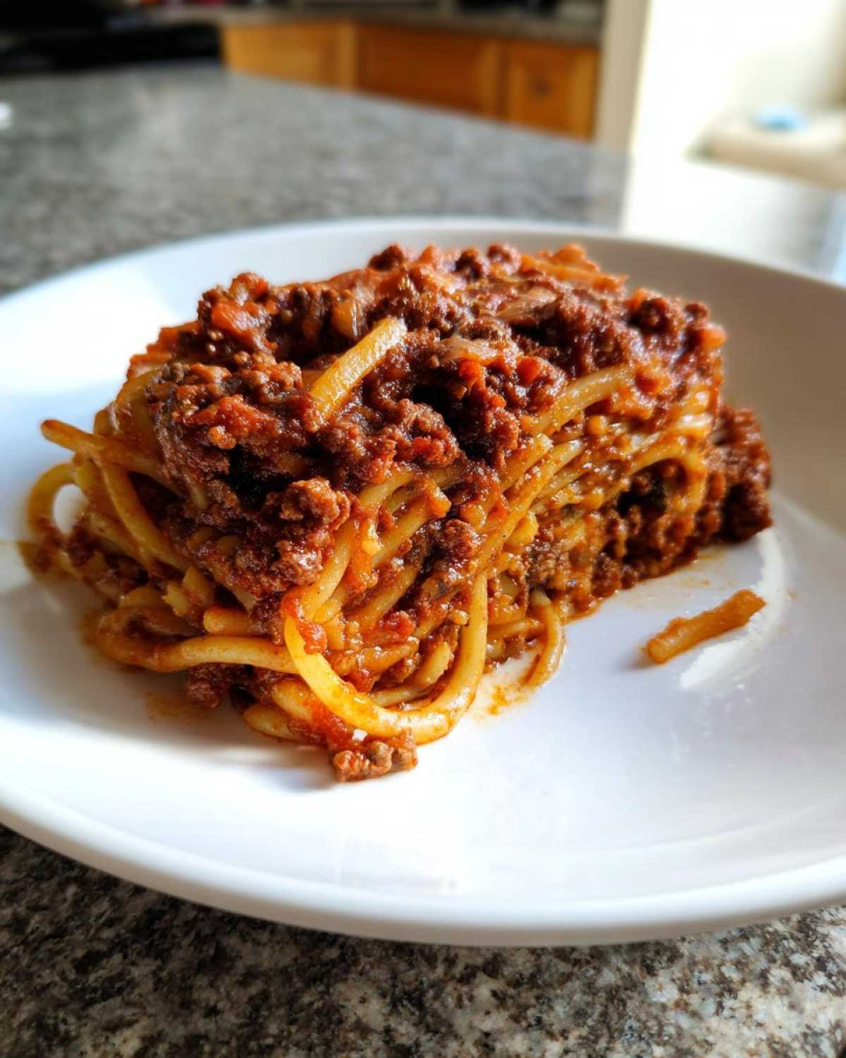 A serving of spaghetti generously coated in rich, meaty bolognese sauce on a white plate.