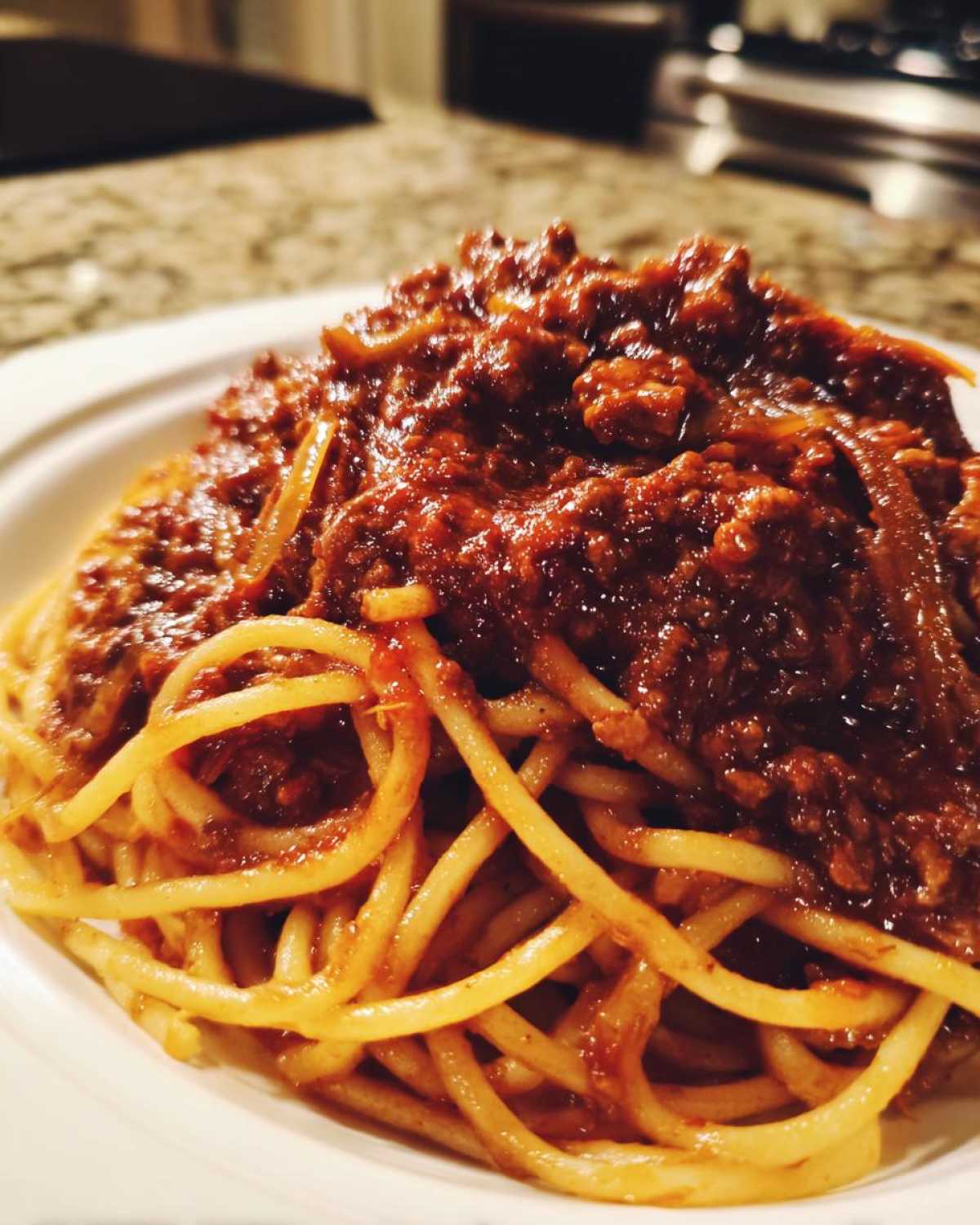 Close-up of spaghetti noodles generously topped with rich, dark red bolognese sauce.