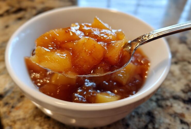 A spoonful of thick, chunky apple pie filling, rich with cinnamon, being lifted from a white bowl.
