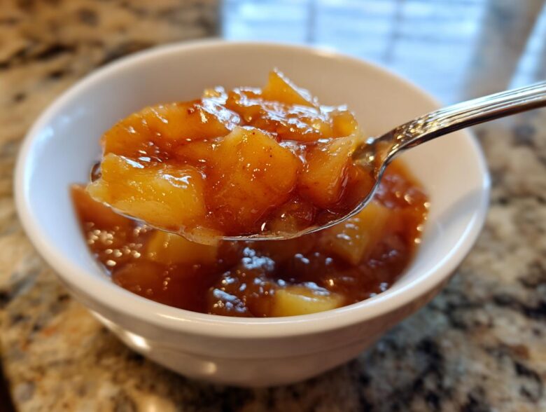 A spoonful of thick, chunky apple pie filling, rich with cinnamon, being lifted from a white bowl.