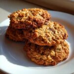A stack of three golden brown, textured oatmeal cookie treats resting on a white plate.