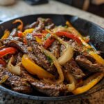 Close-up of sizzling steak fajitas with sliced peppers and onions served in a hot cast iron skillet.