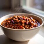 Close-up of a steaming bowl filled with rich, hearty crockpot chili featuring ground meat and kidney beans.