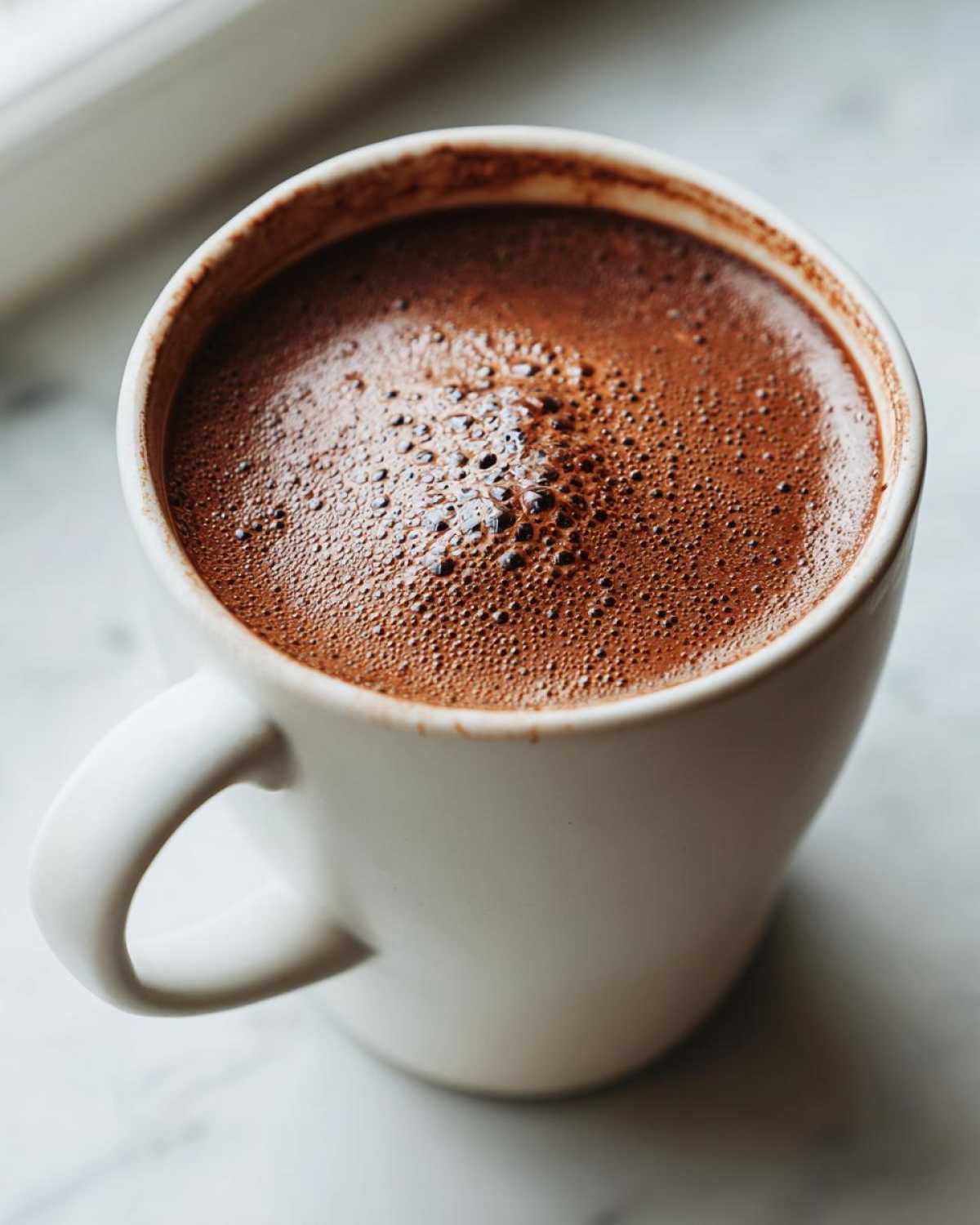 Close-up of a white mug filled with rich, dark hot cocoa topped with small bubbles, made from hot cocoa mix.