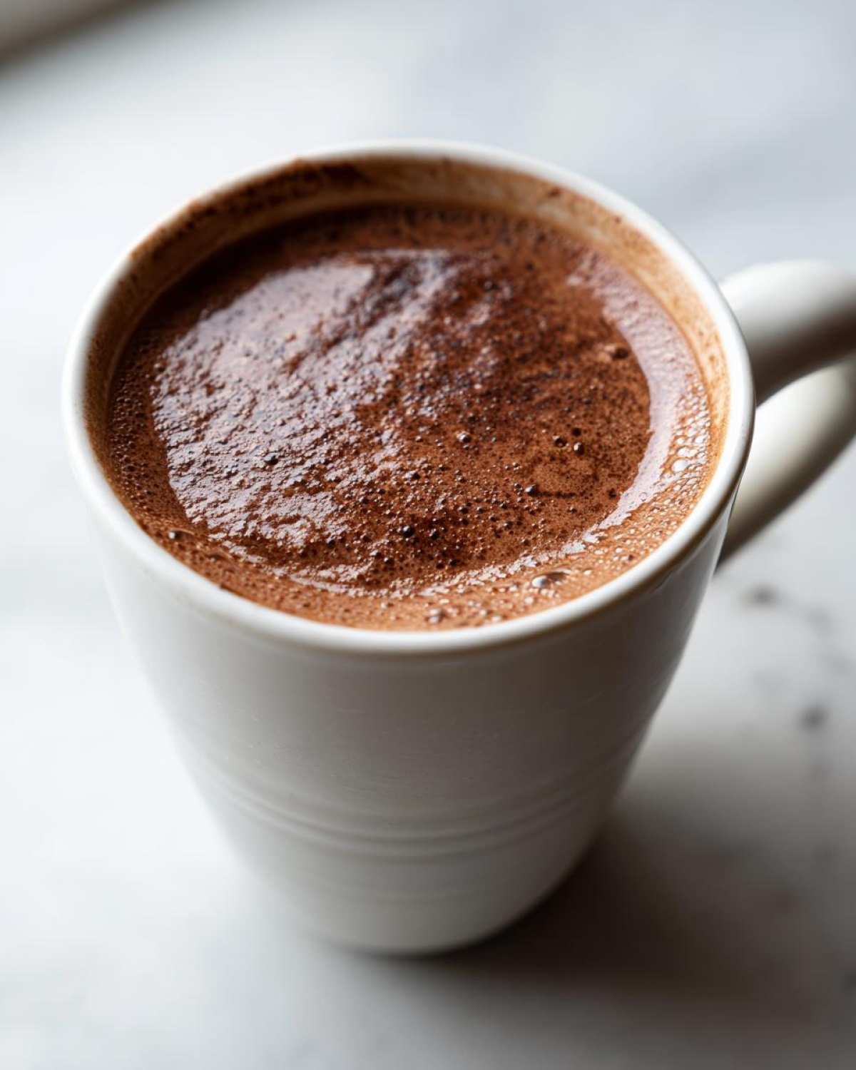 Close-up of a white mug filled with rich, frothy hot cocoa made from homemade hot cocoa mix.