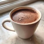 A close-up of a white mug filled with freshly made hot cocoa mix, showing a layer of rich brown foam.