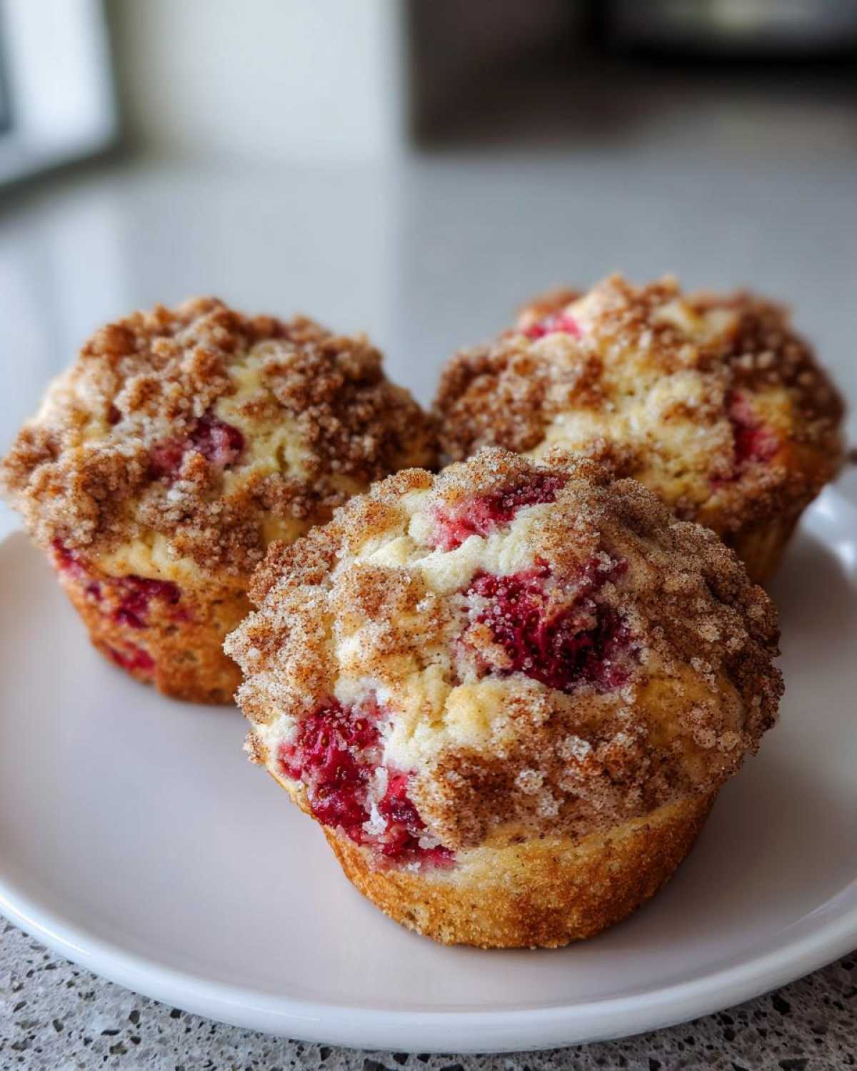 Three moist strawberry muffins topped with a thick cinnamon streusel topping, resting on a white plate.