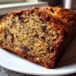 Close-up of a thick slice of moist sugar free banana bread with visible chocolate chips on a white plate.