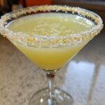 Close-up of a bright yellow lemon drop cocktail in a martini glass with a thick sugar and lemon zest rim.